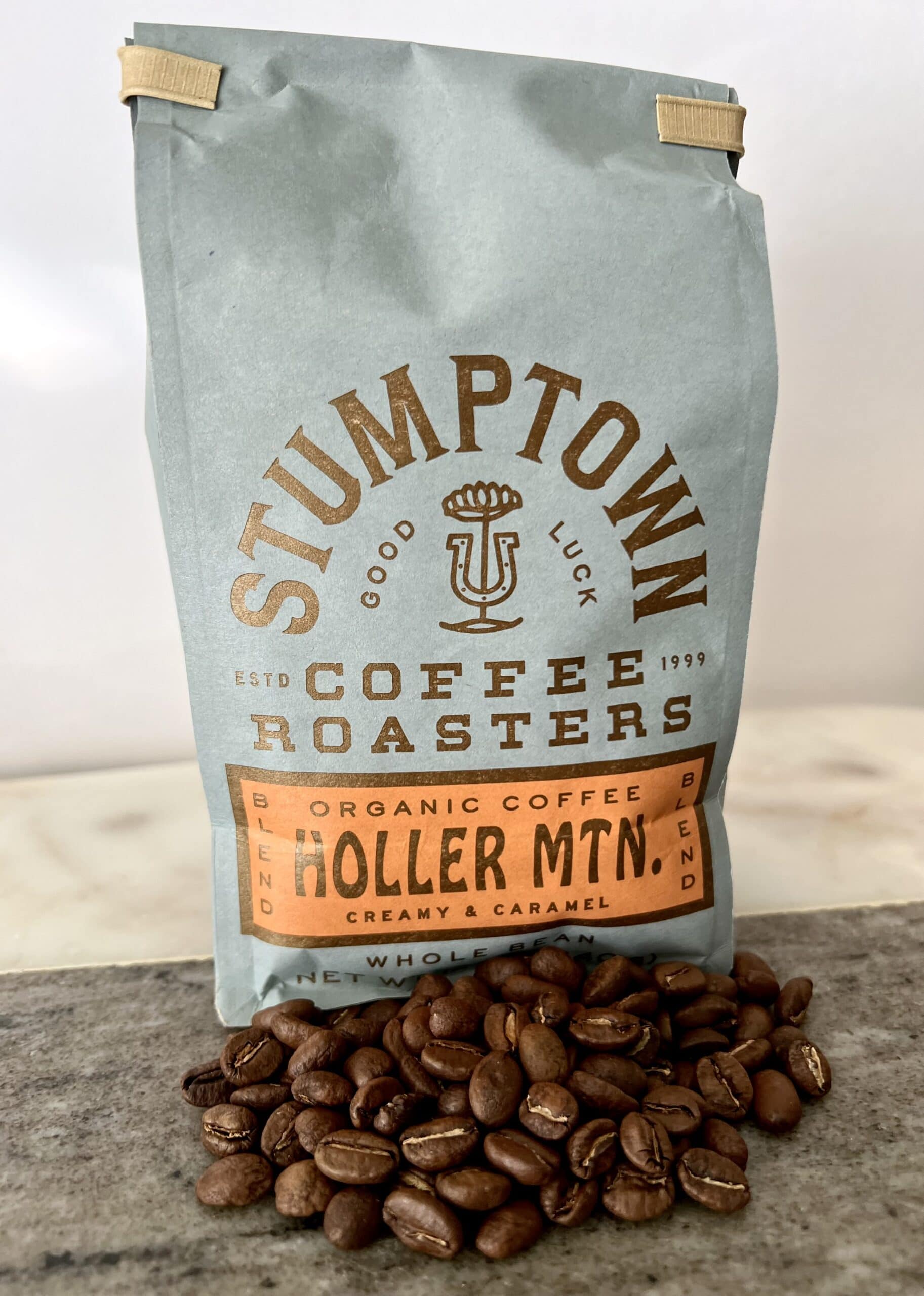 Holler Mountain coffee packaging stands on coffee beans