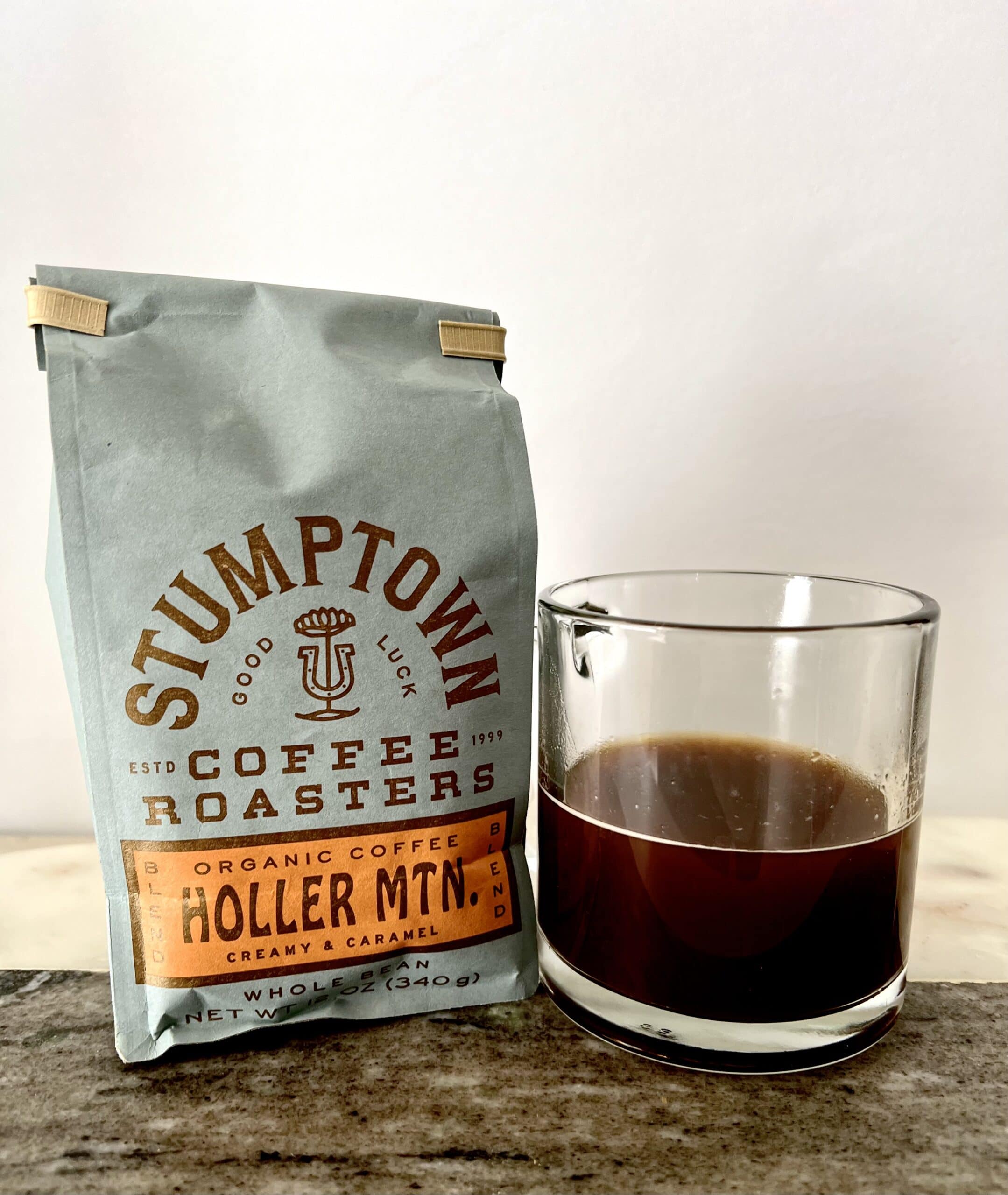 a package of Holler Mountain coffee stands next to a cup of coffee